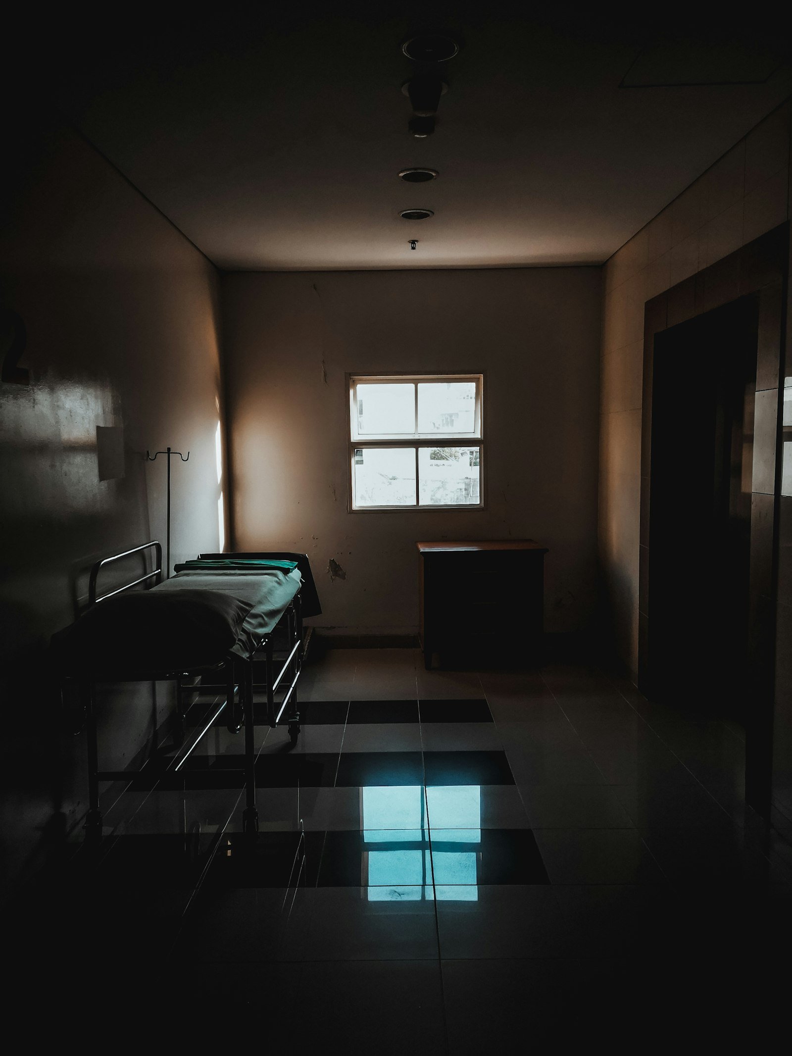 Dimly lit bedroom with bed and window. Photo by fitra zulfy on Unsplash.